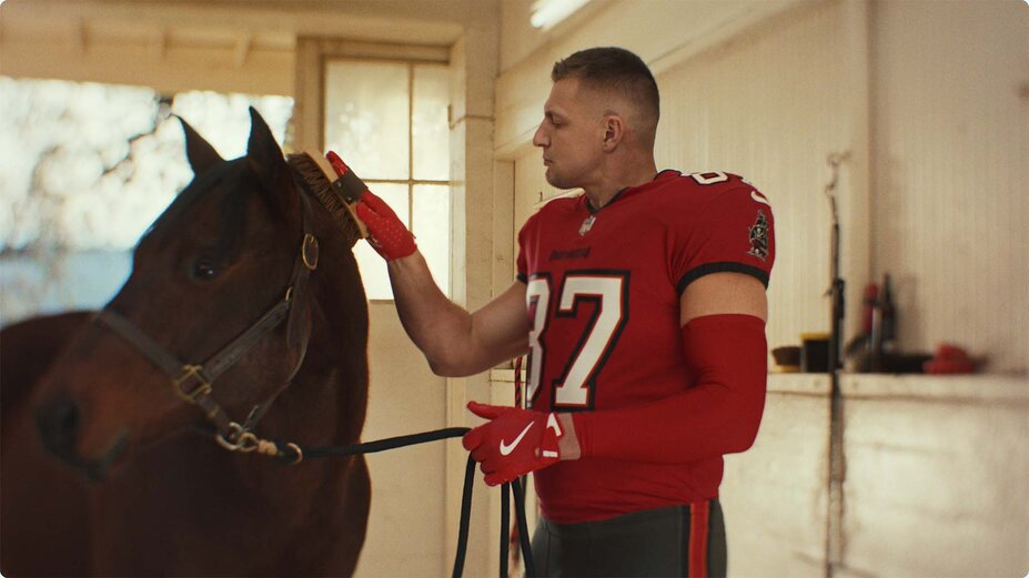 Rob Gronkowski, wearing a Tampa Bay Buccaneers jersey, grooming a horse.